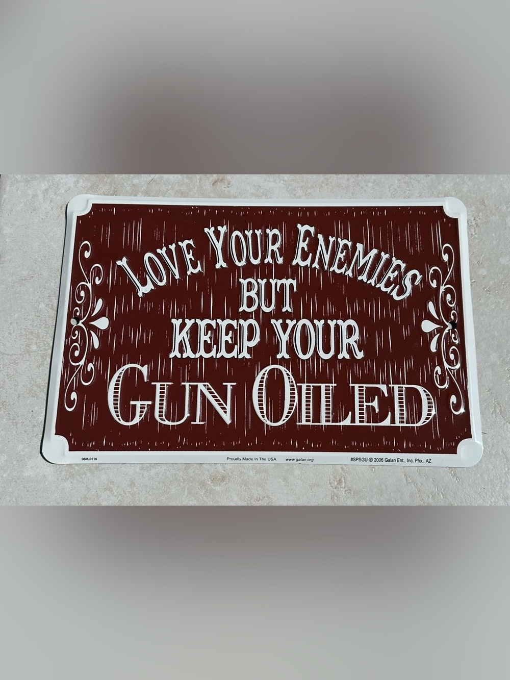 Aluminum sign “Love your enemies but keep your gun oiled”.